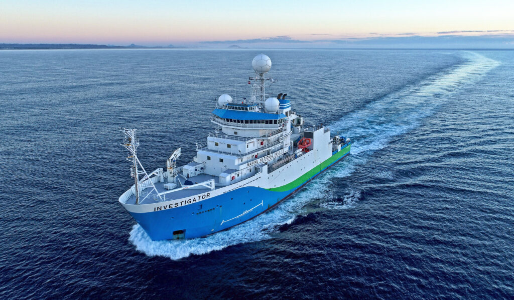 A large ship with a bright blue hull and bright green strip along the side from halfway along its length.