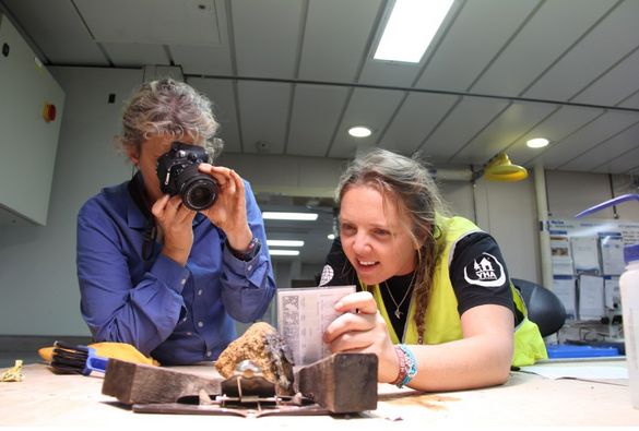 two women look at rock samples while one of them photographs them