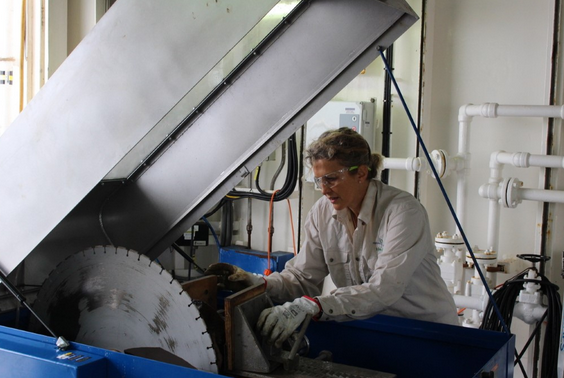 woman in white protective suite, gloves and safety glasses using industrial lathe to cut rock