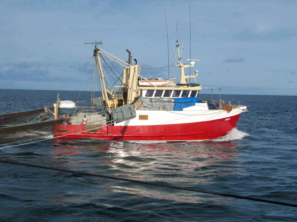 A red and white commercial fishing boat with trawl nets extended behind the vessel.