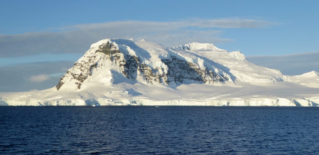 View of Antarctica - the ocean in foreground with mountain encases in snow in distance
