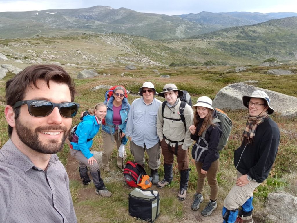 Seven people standing together with Kosciusko National Park mountains as the background.