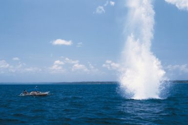 An explosion from fish blasting in the ocean with a small boat near by