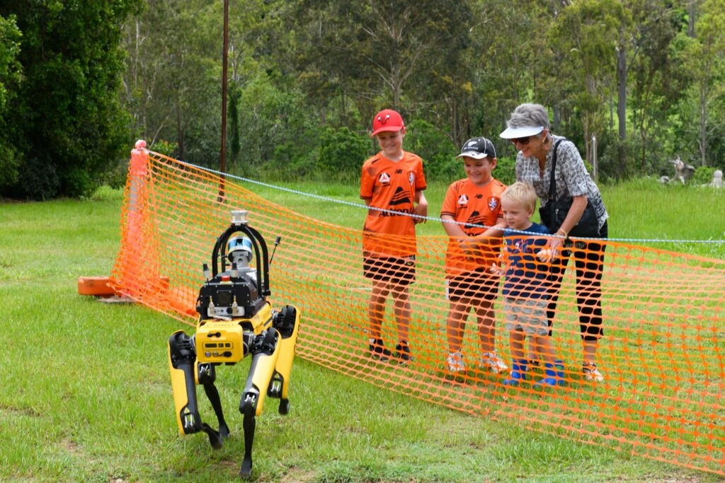 An Adult and 3 children look at a legged robot