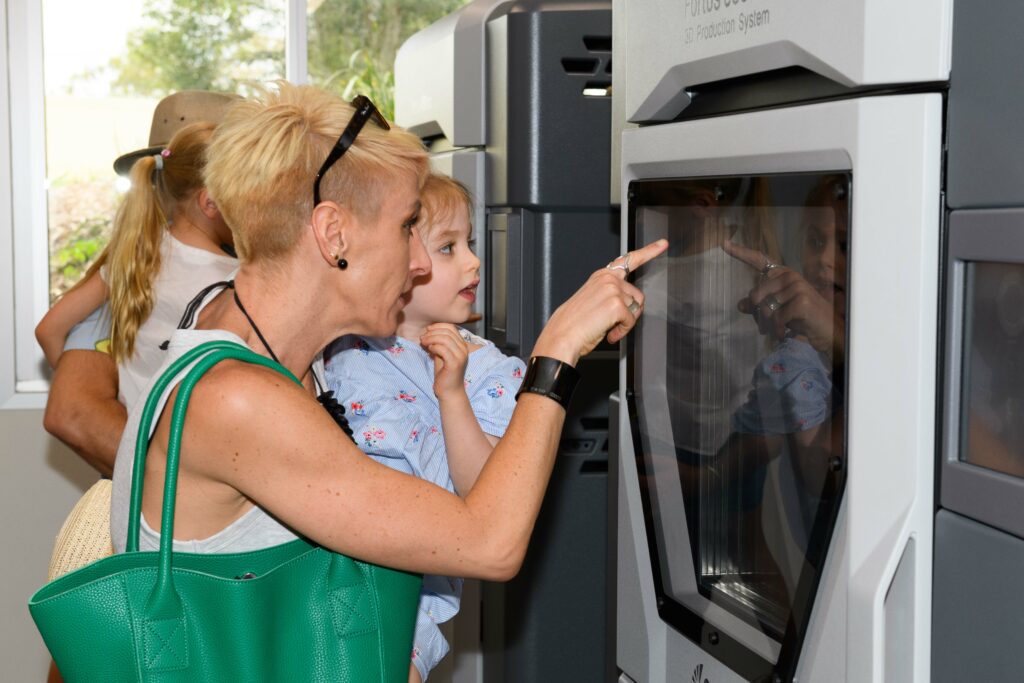 A women holding a child look into a 3D printer