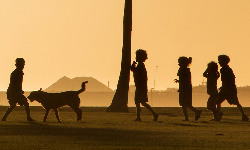 Children playing on the foreshore of an industrial port in the sunset.