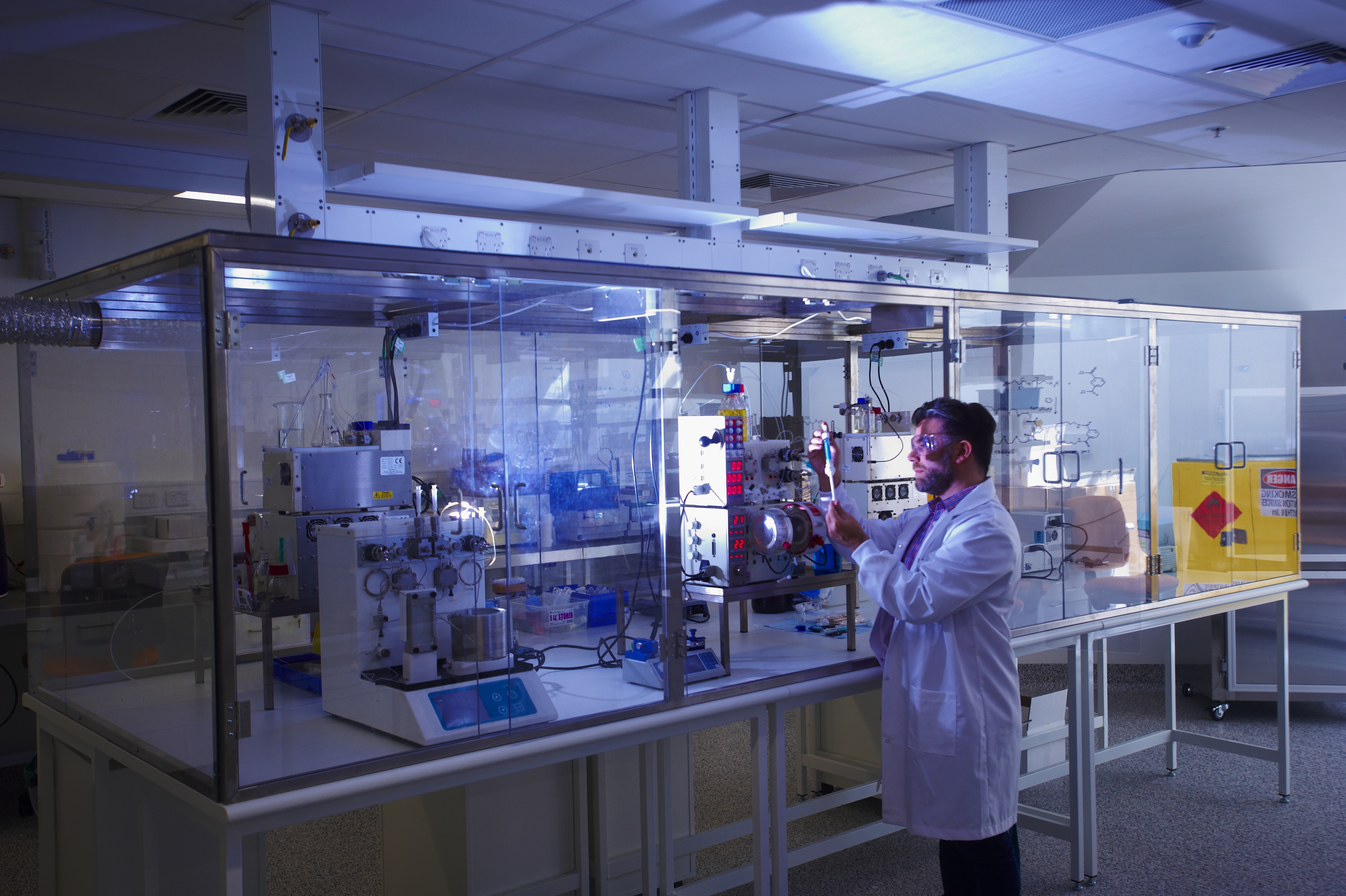 A researcher in a lab coat stands in front of machines in a glass cabinet