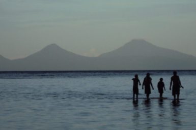 Family standing in the sea across from mountains