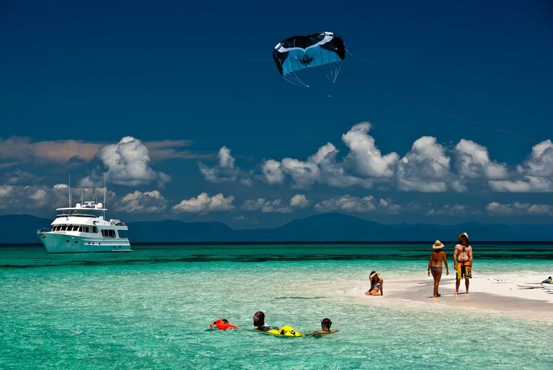 A tropical island beach with swimmers. a boat and a parasail