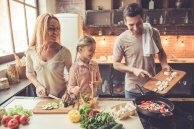 Girl and her parents are smiling while cooking in kitchen at home